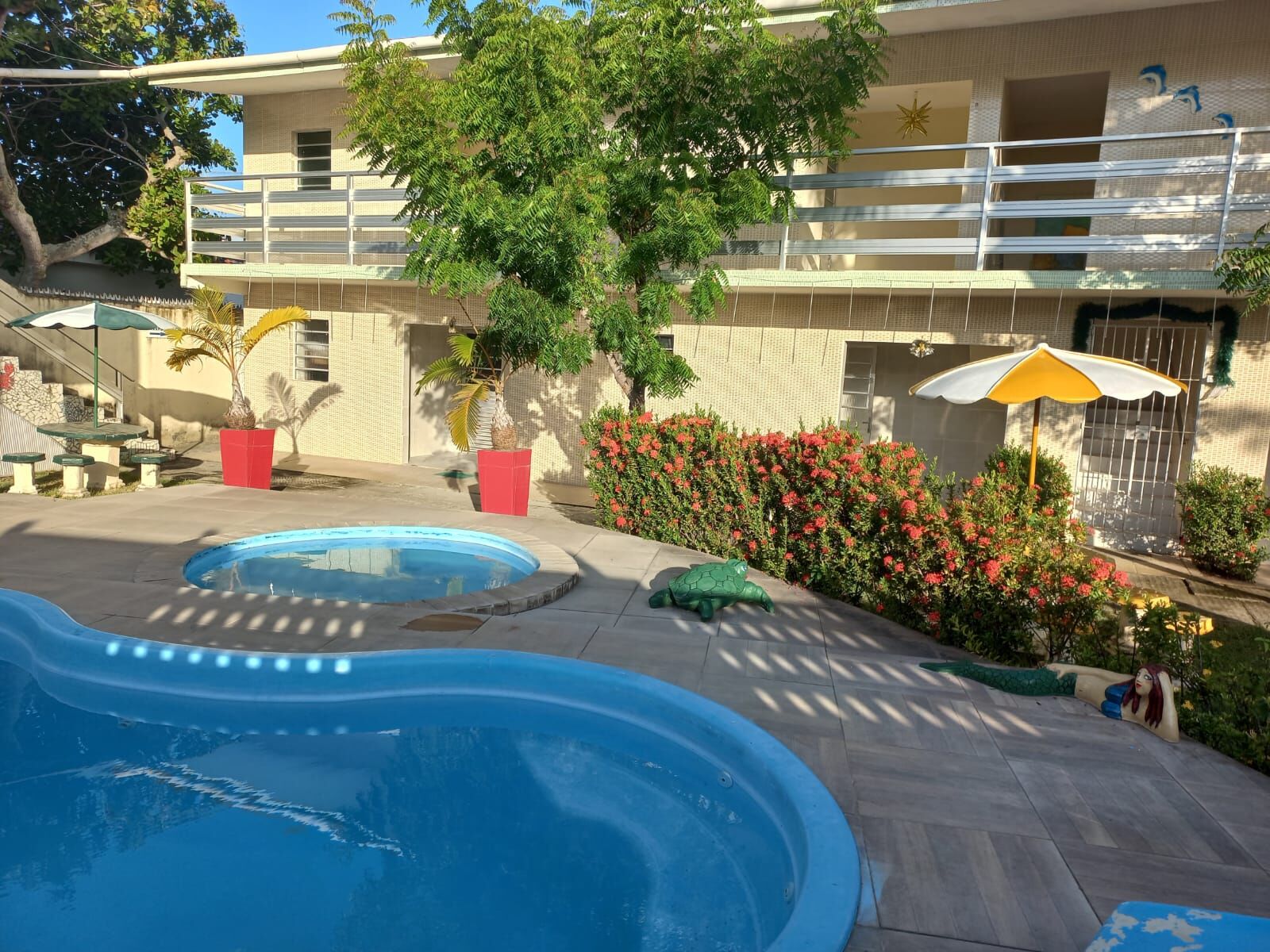 Vista da piscina com jardim de ixoras e estátua de sereia